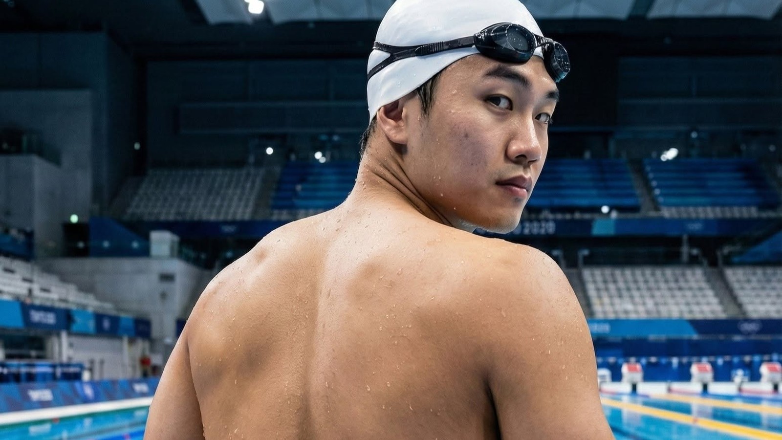 An ngồi mép hồ, mũ trắng, kính gác trên trán, quay lại nhìn.