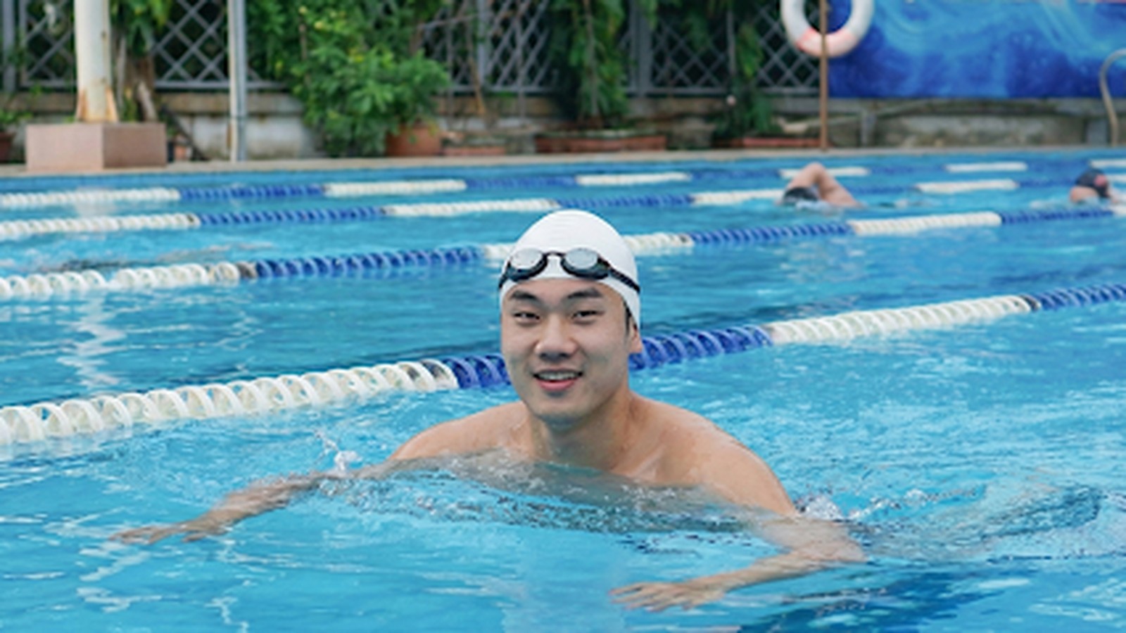 An đứng trong làn, mũ trắng, kính gác trán, hai tay đặt trên mặt nước.